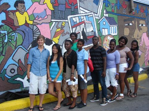 Colour photograph of a group of teenagers from different racial groups standing in front of a coloured mural representing the multicultural and inclusive character of the place.