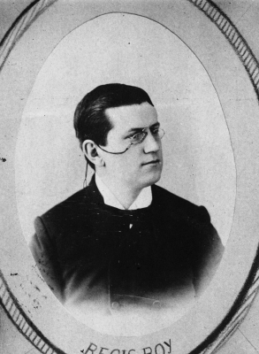 Black and white studio photograph of a mature man. He wears a three-piece suit, bow tie and glasses. His salt and pepper hair is combed back. He wears a serious expression.